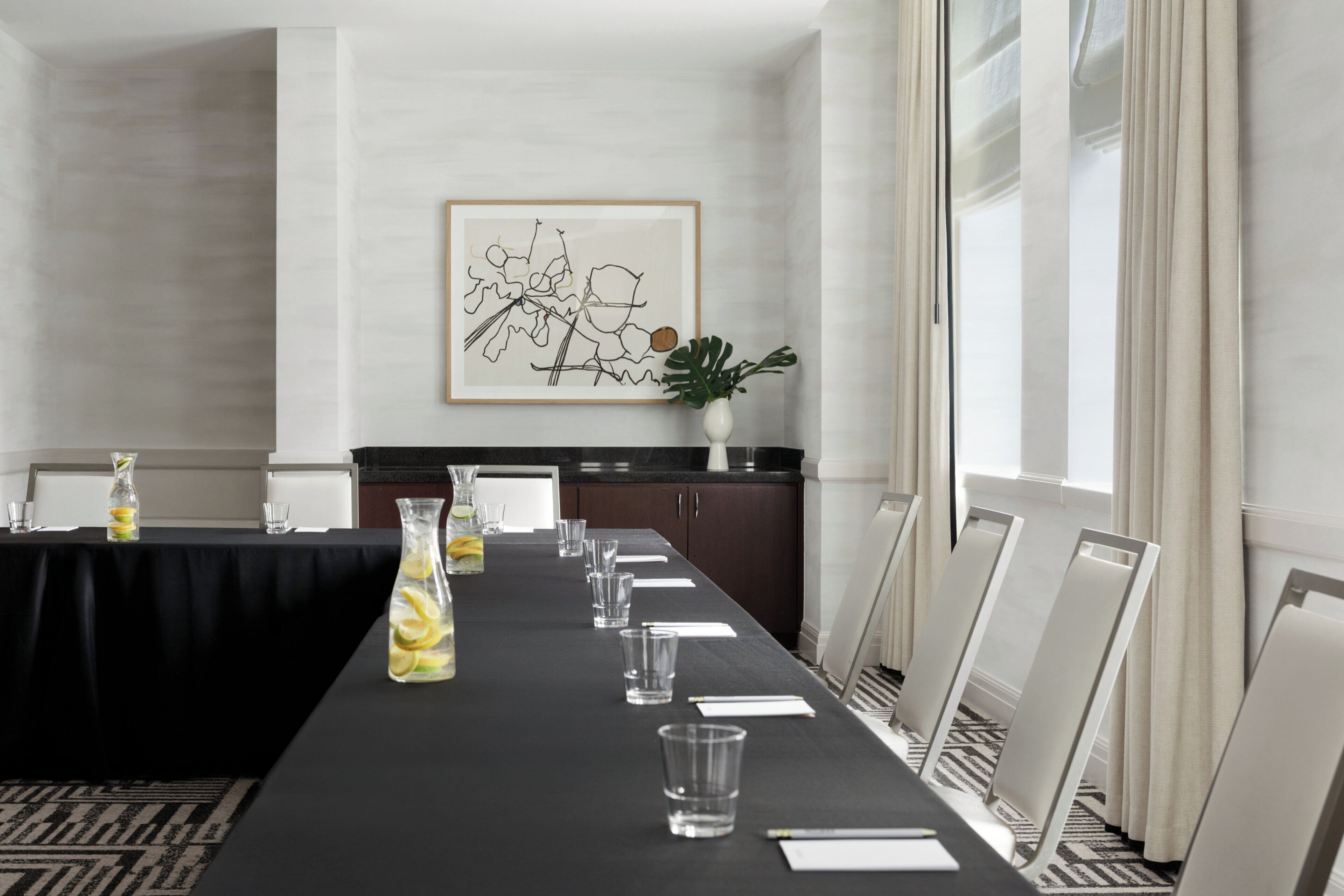 A conference room with a long table, chairs, a vase with a plant, and a framed artwork on the wall.