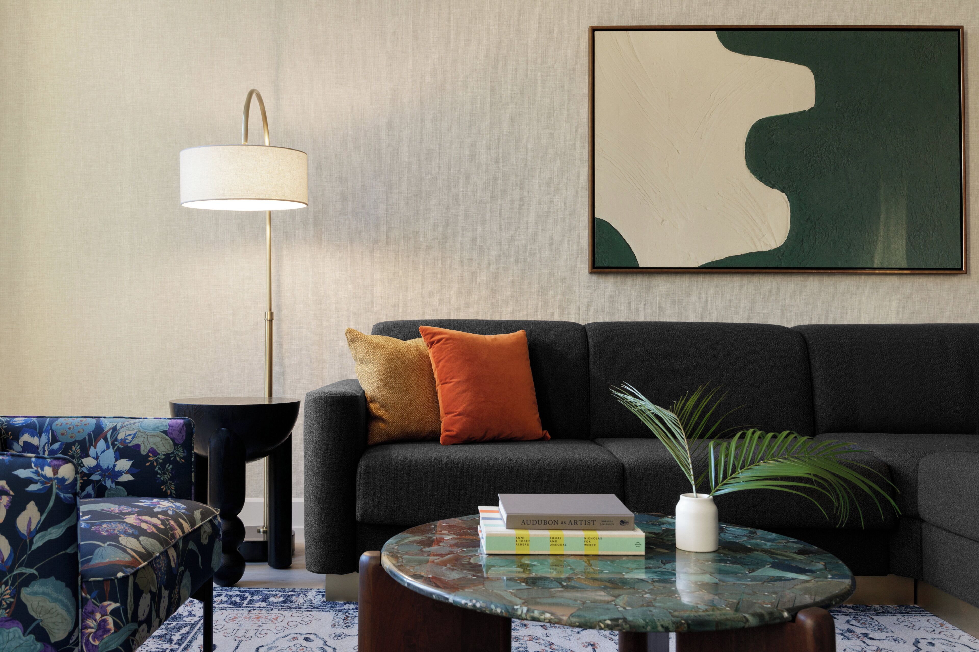 Ein Wohnzimmer mit einer Couch, einem runden Couchtisch, einer Stehlampe, einem gemusterten Sessel und einem gerahmten abstrakten Gemälde.