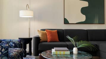 Ein Wohnzimmer mit einer Couch, einem runden Couchtisch, einer Stehlampe, einem gemusterten Sessel und einem gerahmten abstrakten Gemälde.