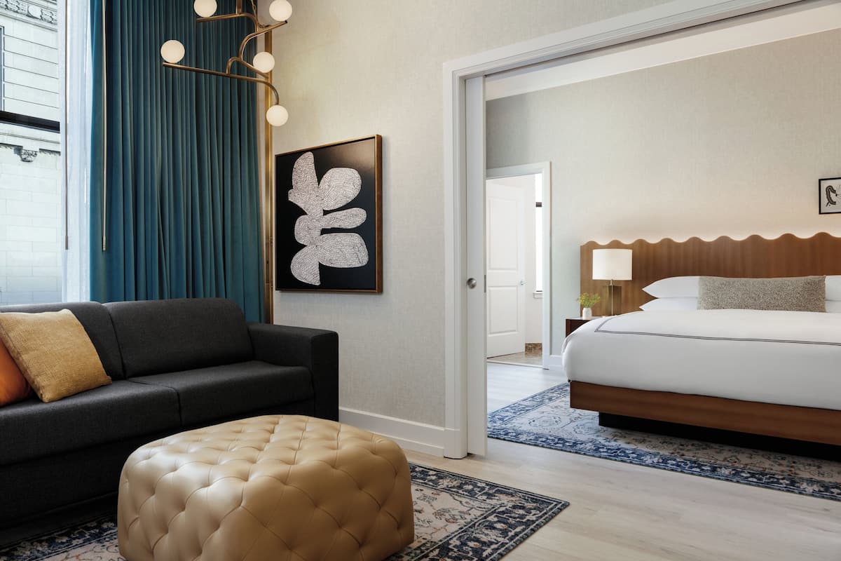 Una habitación de hotel con una cama, un sofá, un adorno en la pared y una puerta que da a otra estancia.