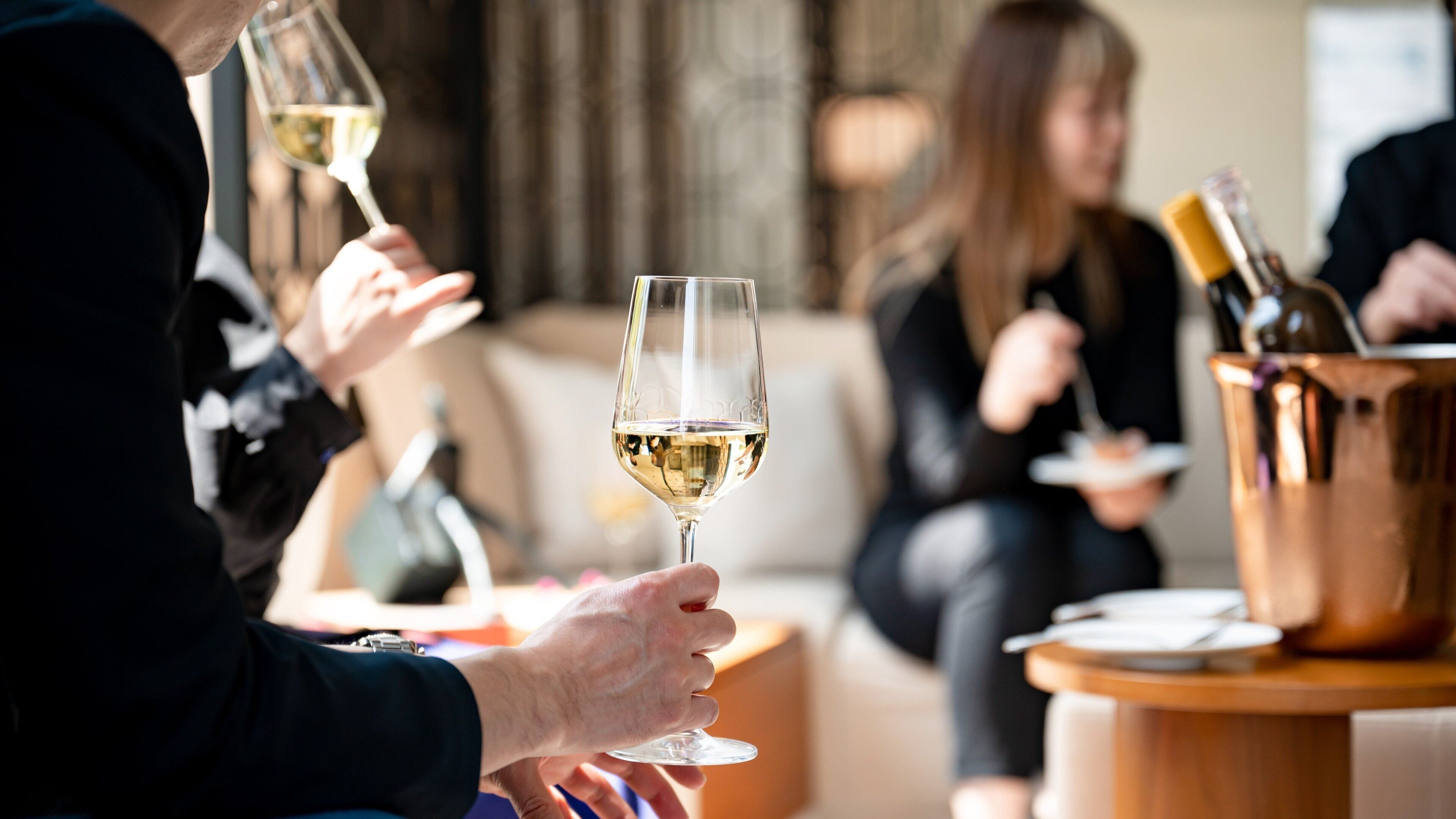 A group of people holding wine glasses, seated around a table with a copper wine bucket.