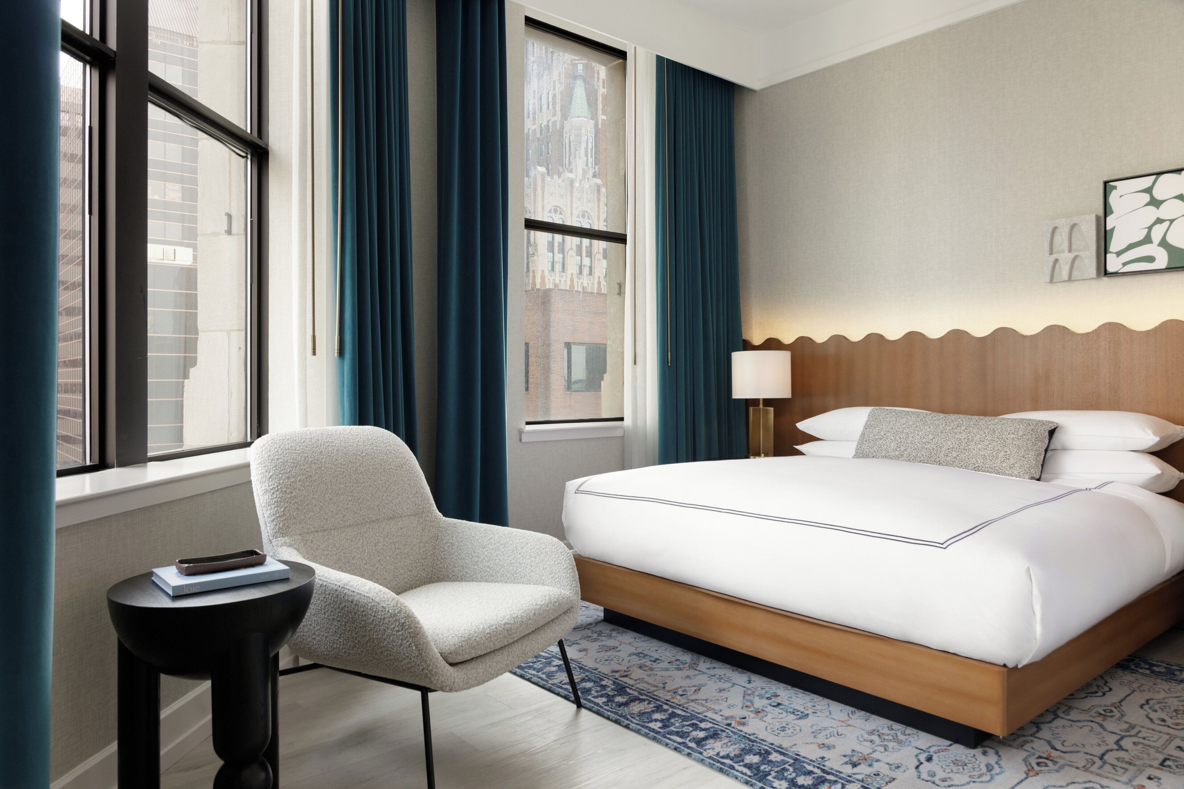 Habitación de hotel con cama, una silla, una mesita y ventana con cortinas.