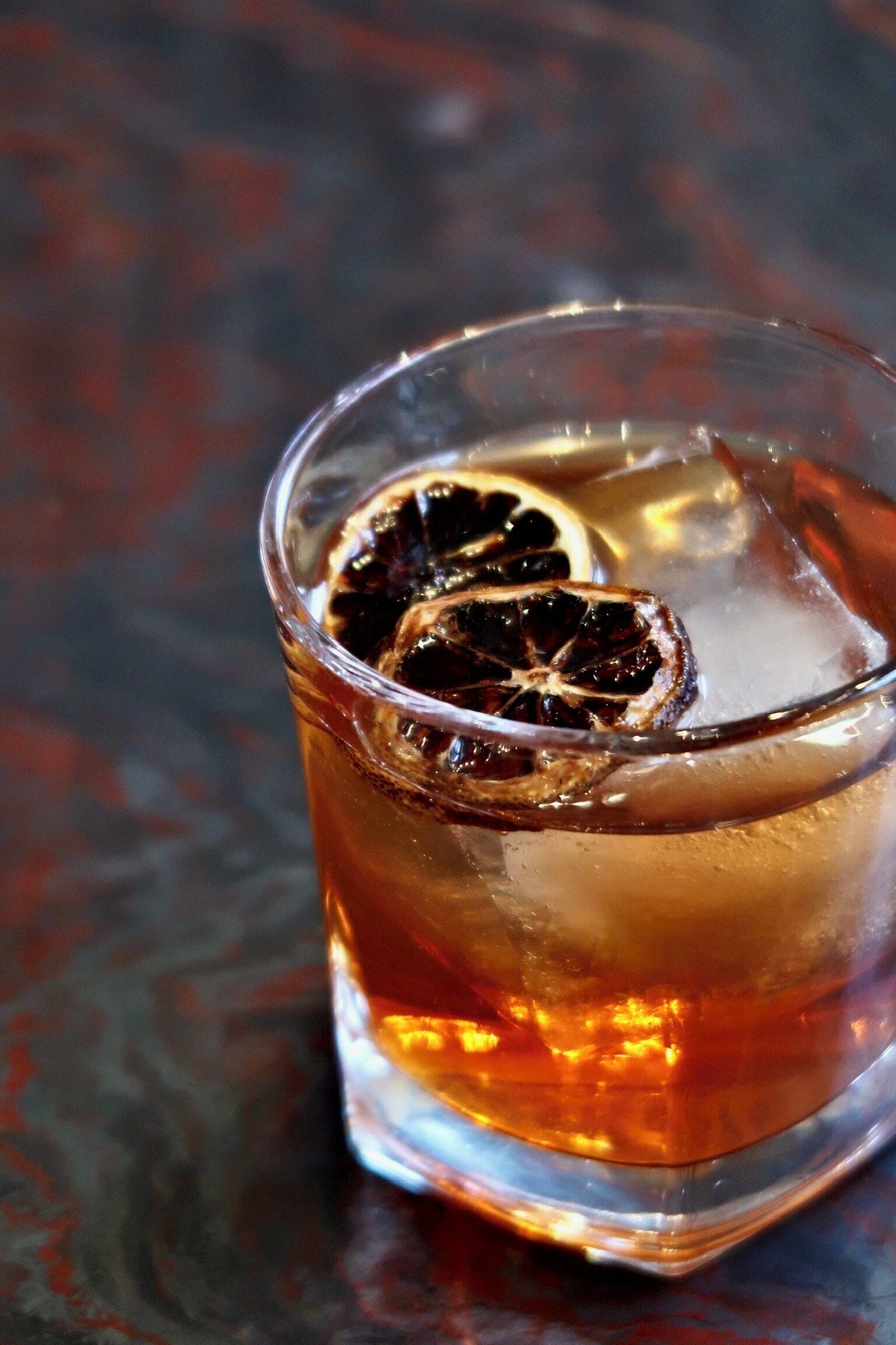 Un vaso con líquido oscuro, hielo y una rodaja de naranja deshidratada.