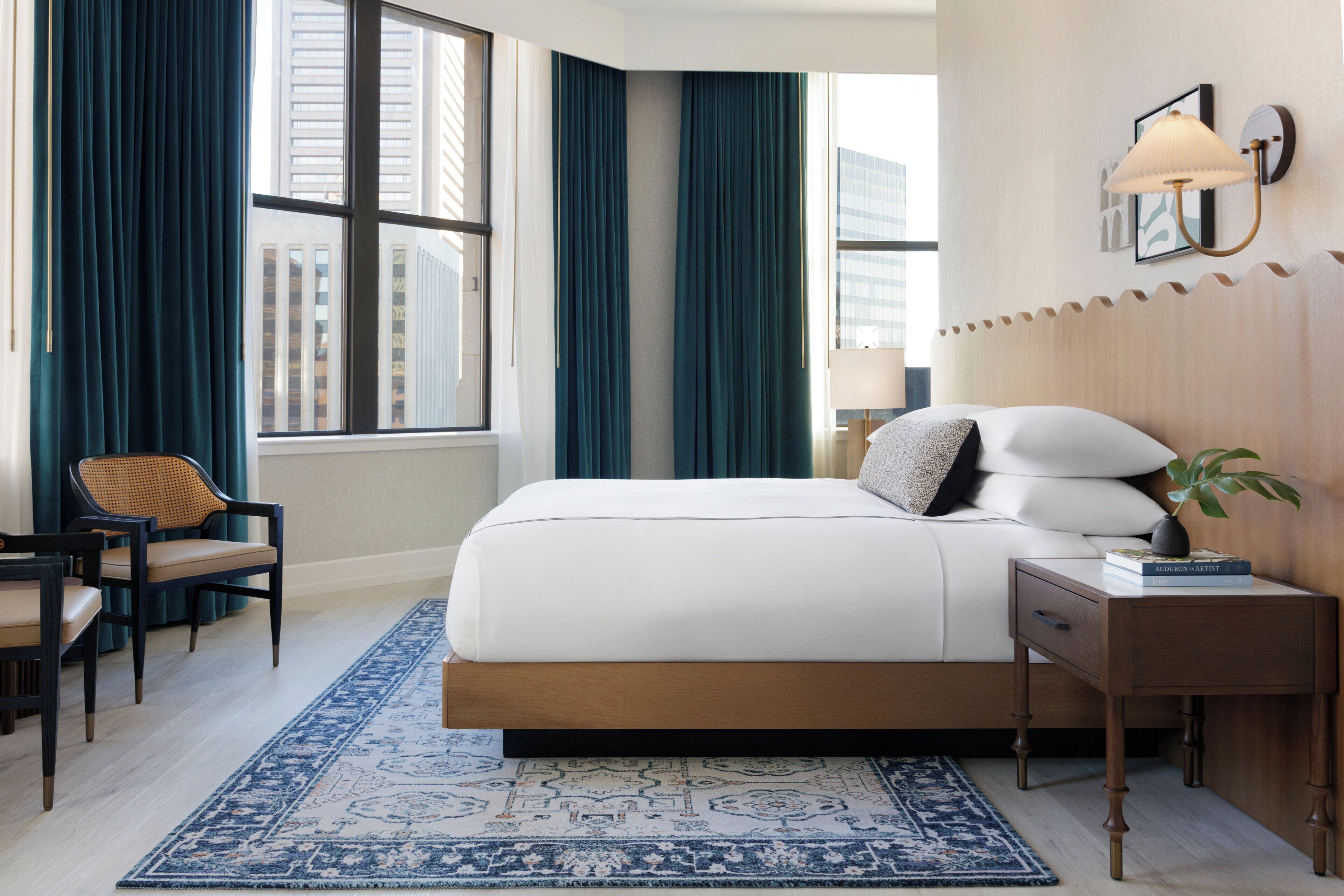 A hotel room with a large bed, a desk, a chair, a nightstand, and a window with curtains.