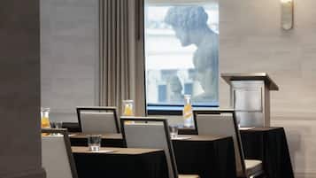 Ett konferensrum med en stor projektionsduk, bord med stolar och en staty i bakgrunden.