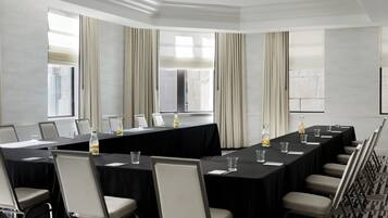A conference room with a long table, chairs, a projector screen, and large windows with curtains.