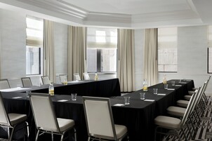 A conference room with a long table, chairs, a projector screen, and large windows with curtains.