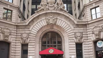 A building with a classical architectural style, featuring a prominent arched entrance with a red awning and a crest above it.
