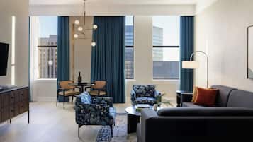 A modern living room with a sofa, armchairs, a coffee table, a TV, and a dining area with chairs and a table.