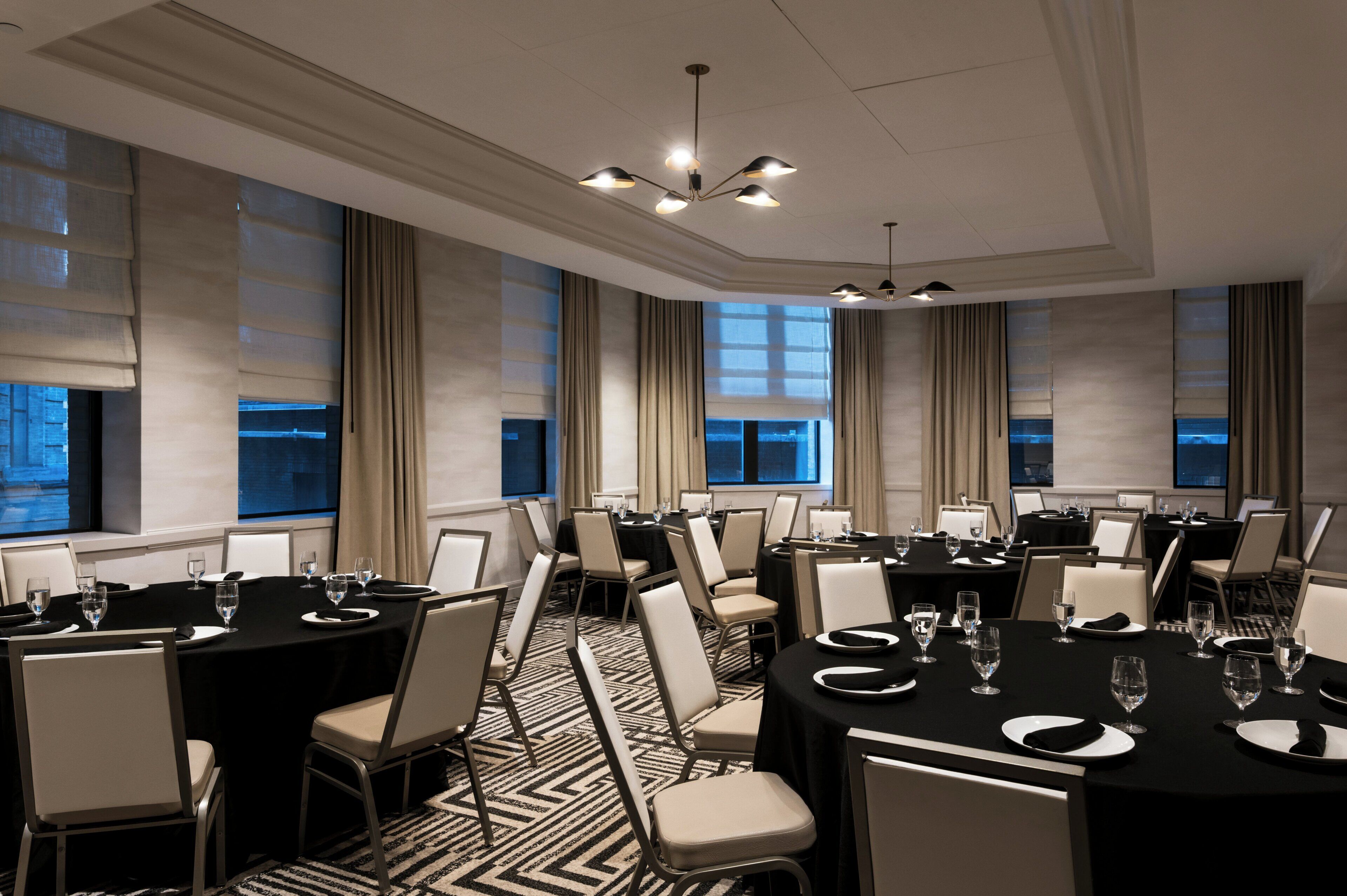A conference room with multiple tables set for meetings, equipped with chairs and tables, and large windows with curtains.
