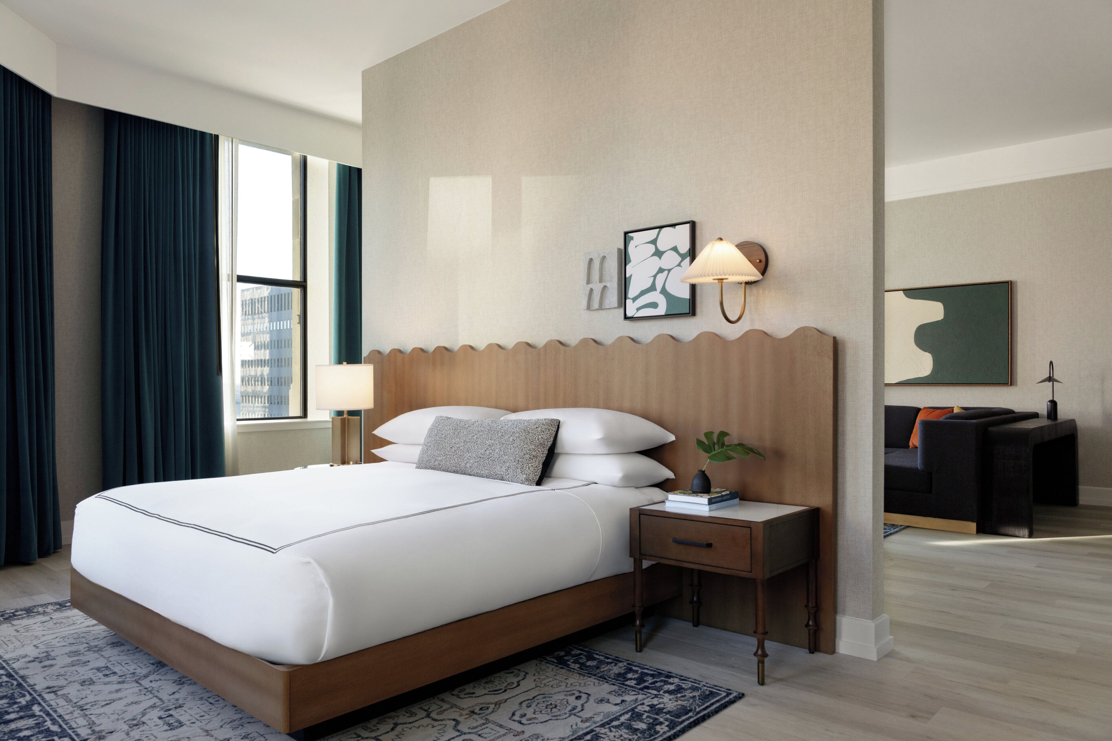 A modern hotel room with a large bed, a bedside table, a desk, and a view of the city.