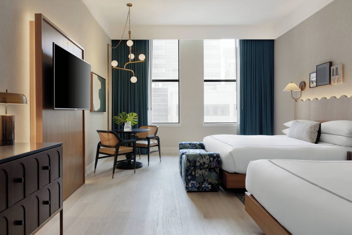 Habitación de hotel con cama, escritorio, silla, televisión y ventana.