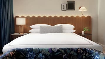 A hotel room with a bed, a nightstand, a lamp, a wall-mounted picture, and a small table with a plant.
