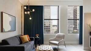 Ein modernes Wohnzimmer mit Sofa, Sessel, Hocker und einer Deckenleuchte.