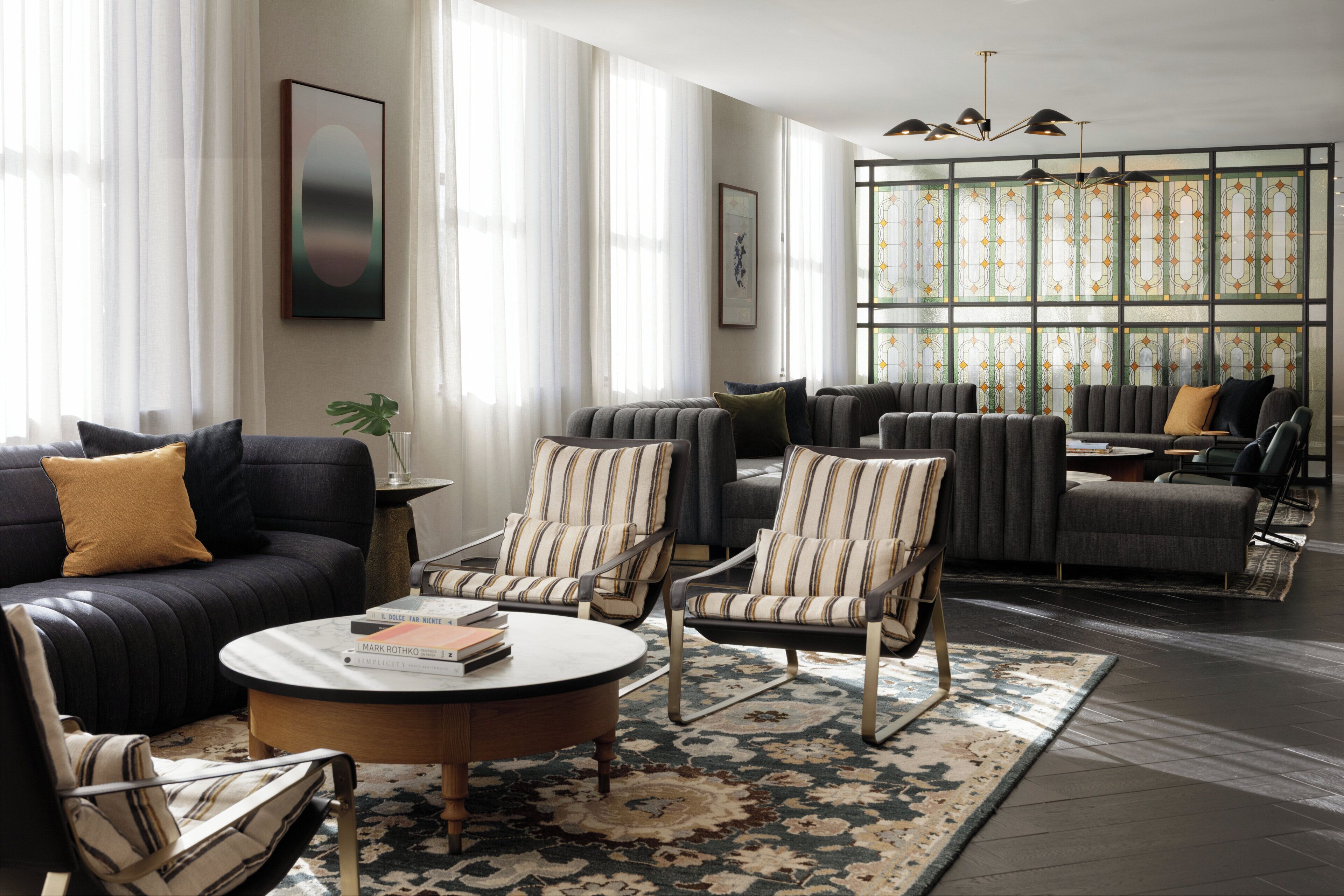 Ein modernes Wohnzimmer mit einem dunklen Sofa, gestreiften Sesseln, einem runden Couchtisch und einem großen Fenster mit gemustertem Glas.