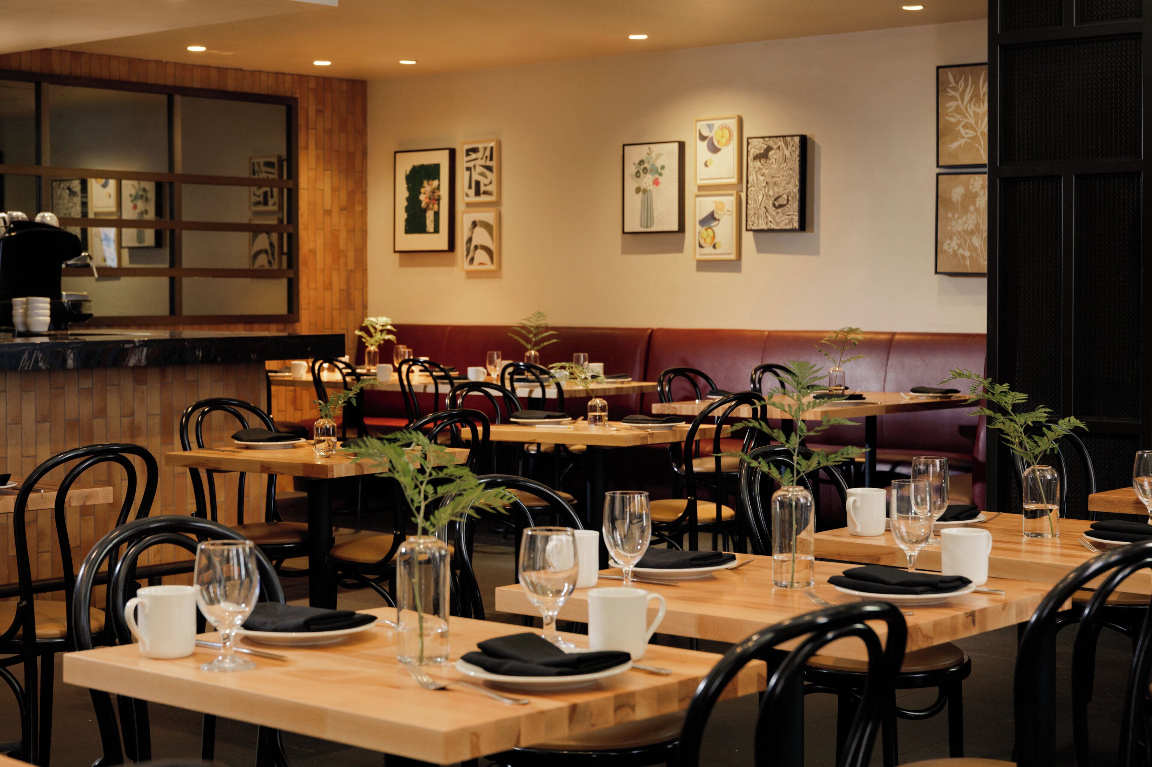 A restaurant interior with wooden tables, black chairs, and various framed artworks on the walls.