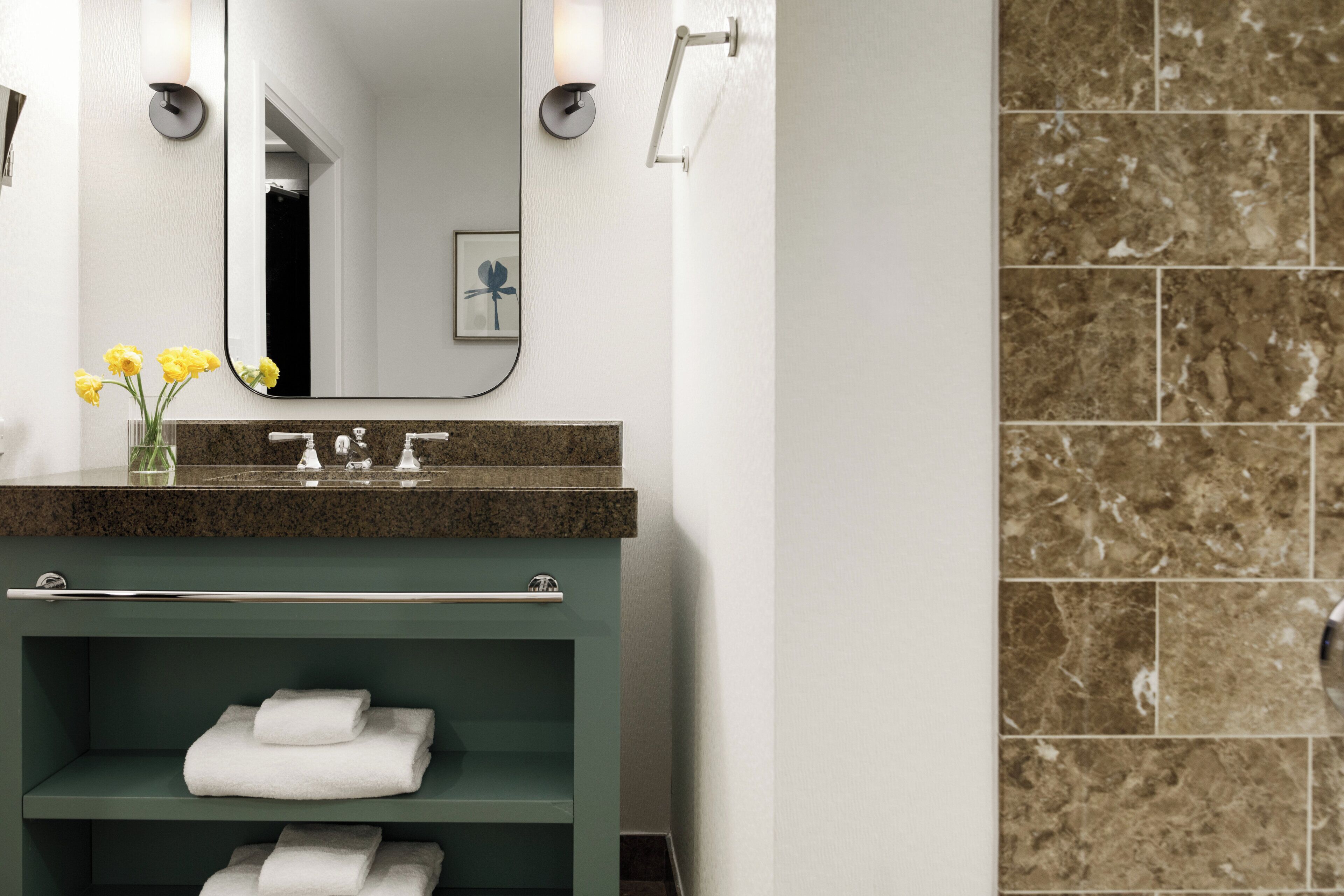 A bathroom with a granite countertop, a green vanity, a mirror, and a towel rack.
