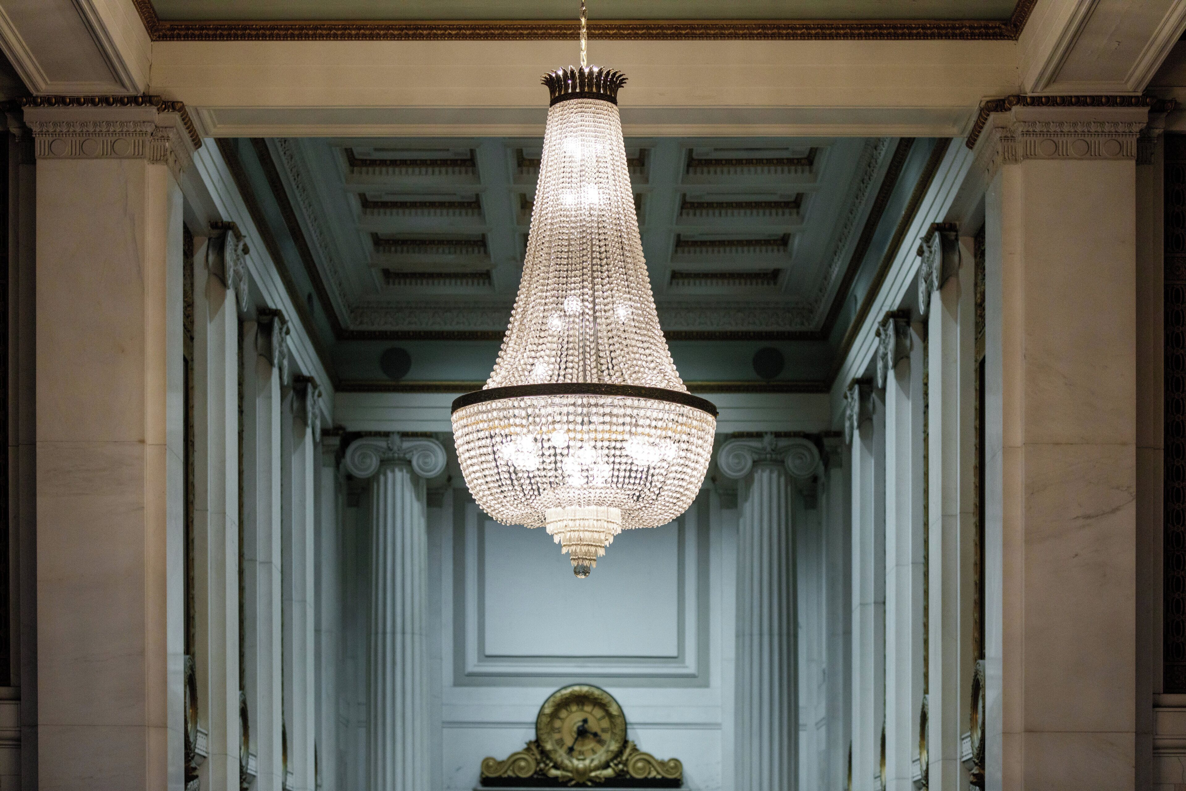 A grand hallway with a large, ornate chandelier and a clock on the wall.