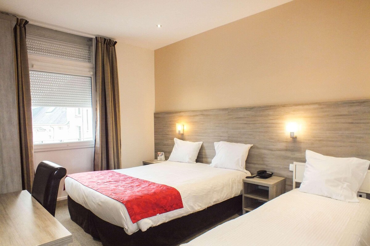 A hotel room with a bed, bedside tables, a desk, and a chair.