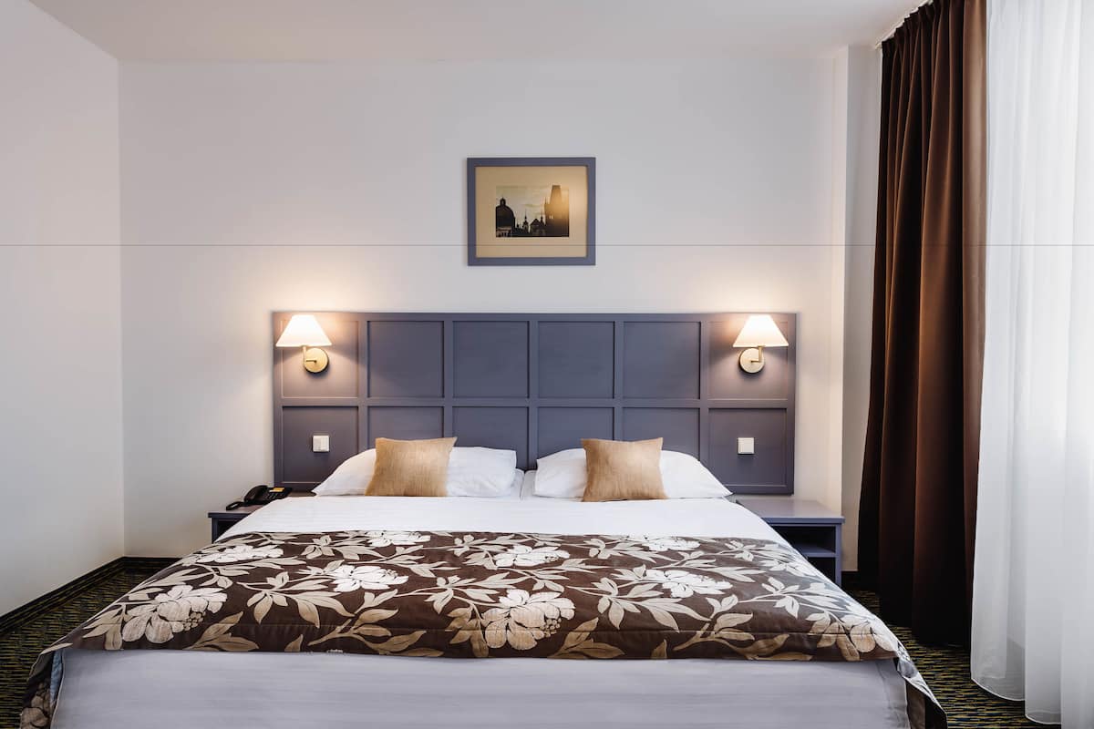 A hotel room with a bed, two bedside lamps, a framed picture on the wall, and a window with curtains.