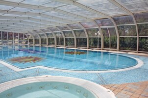 Una piscina techada, una piscina al aire libre, sombrillas