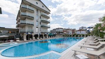 Ein Pool mit Liegestühlen und Sonnenschirmen, umgeben von einem mehrstöckigen Gebäude mit Balkonen.