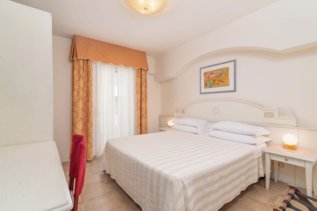 Une chambre d’hôtel avec un lit, des tables de chevet, un bureau et un tableau au mur.