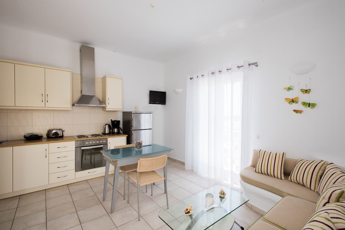 A modern kitchen with white cabinets, a glass dining table, and a sofa with striped cushions.