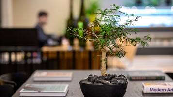 A table with a bonsai tree in a black bowl, surrounded by magazines and books.