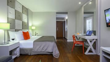Habitación de hotel moderna con cama, escritorio, silla, televisión y baño visible a través de una puerta abierta.