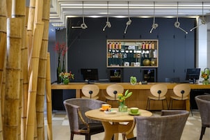 Un moderno bar con mostrador de madera, taburetes y una zona de estar con mesas redondas y sillas de mimbre.