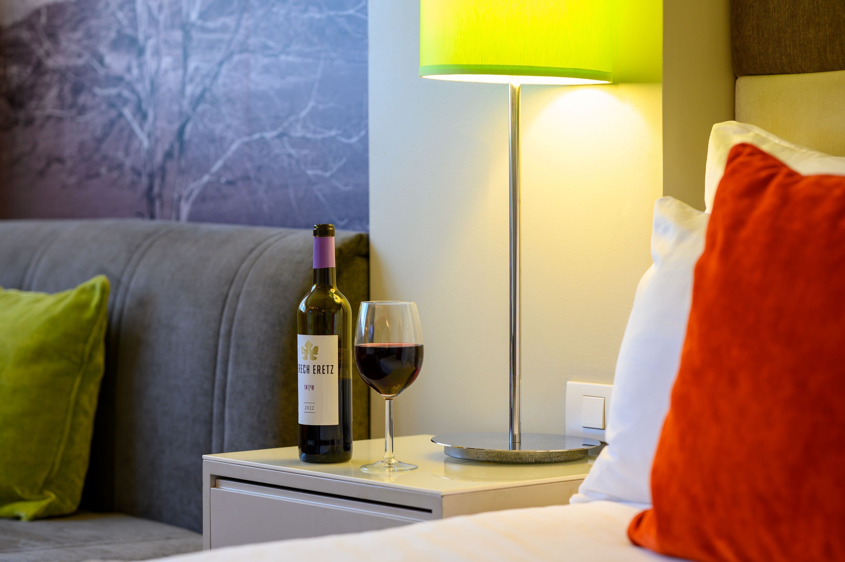 A hotel room with a bed, a nightstand, a wine bottle, and a wine glass.