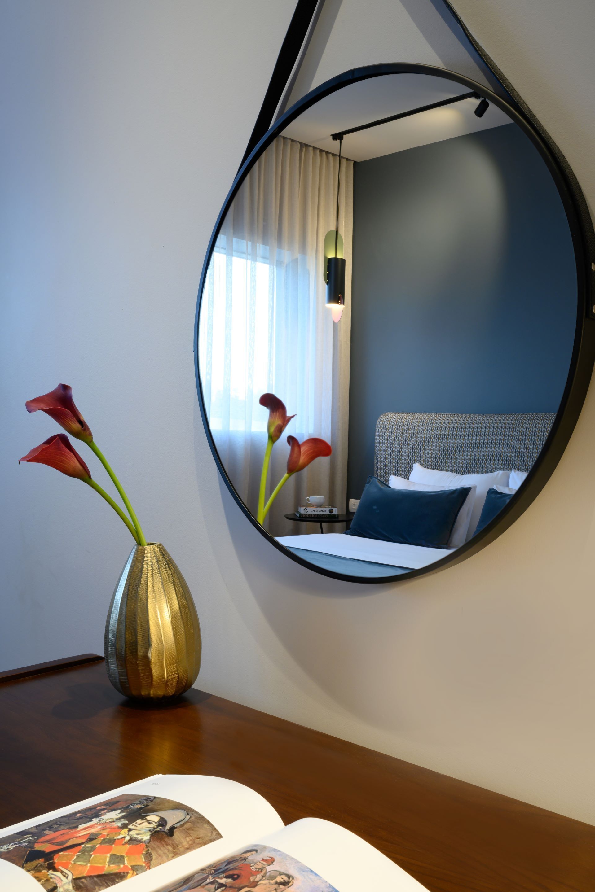 Ein Hotelzimmer mit Bett, Nachttisch, Spiegel und einer Vase mit Blumen.