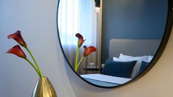 Ein Hotelzimmer mit Bett, Nachttisch, Spiegel und einer Vase mit Blumen.