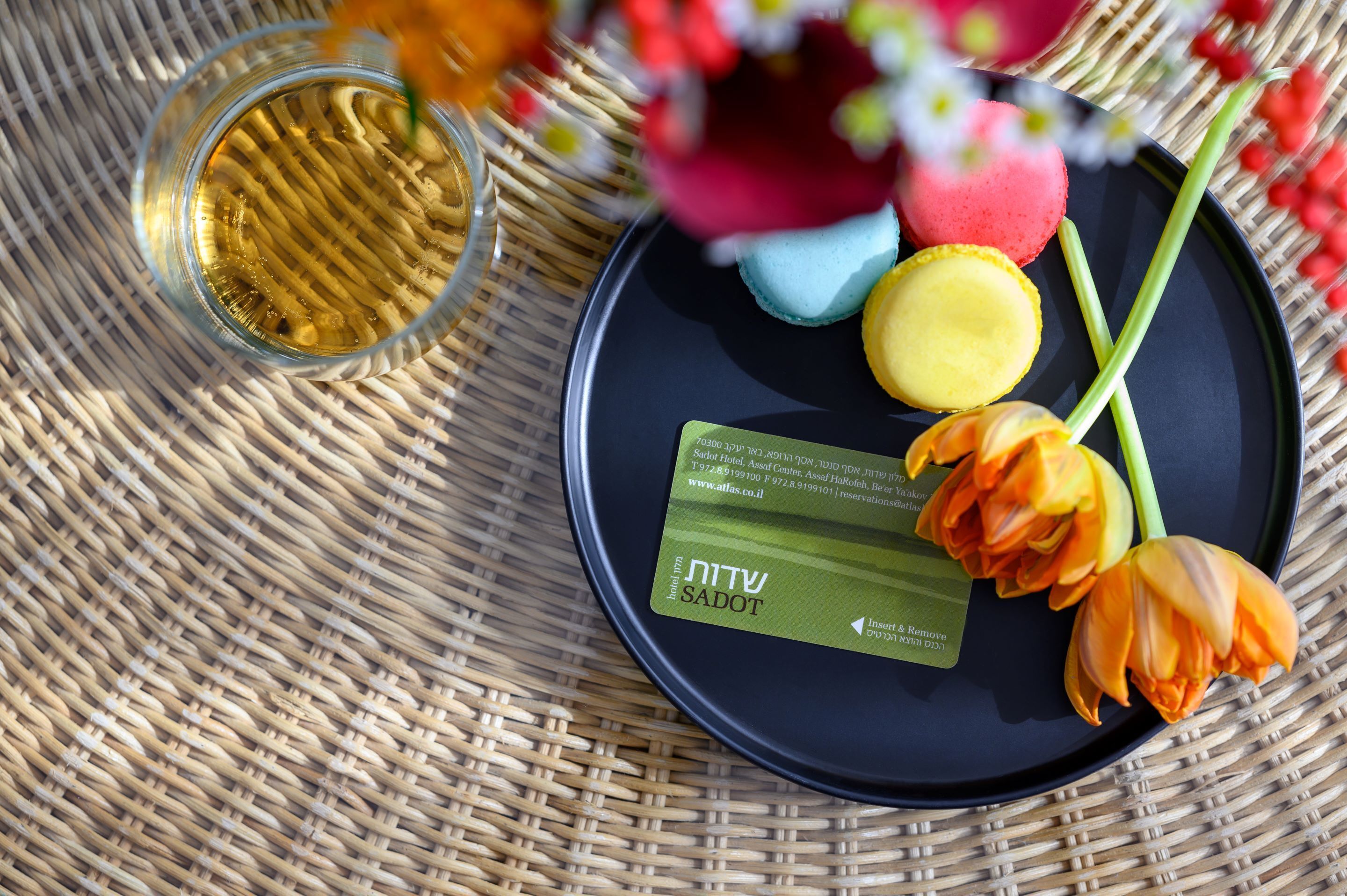 A black plate with macarons, a glass of liquid, and a green card on a woven mat.