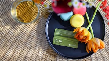 A black plate with macarons, a glass of liquid, and a green card on a woven mat.