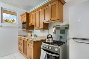 Una cocina con armarios de madera, estufa, microondas y ventana con vistas a plantas.