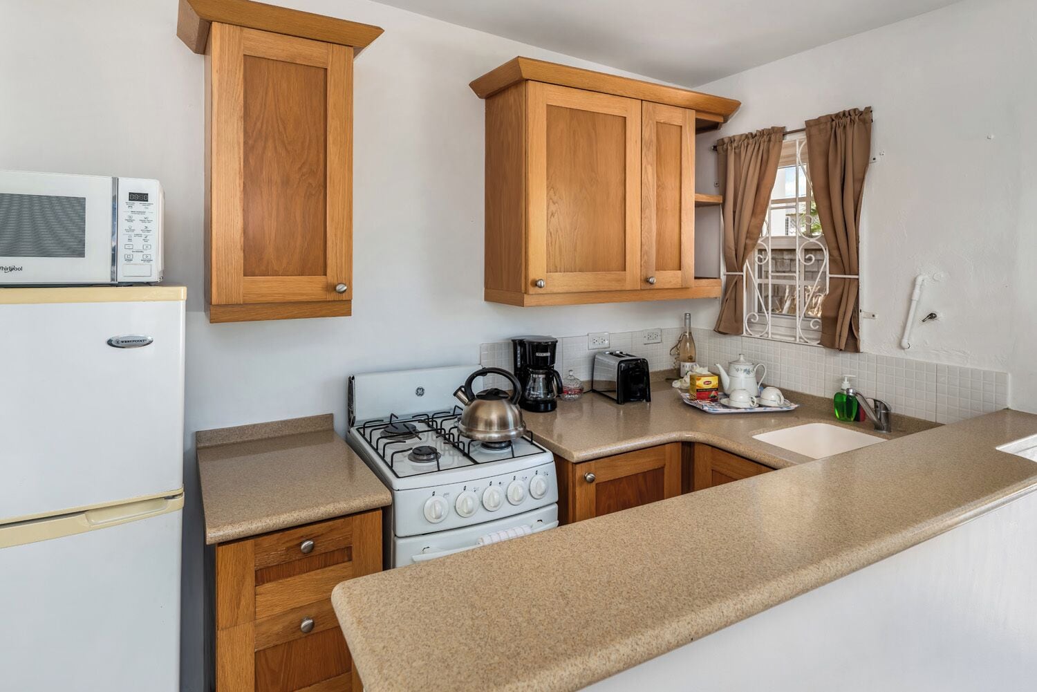 A compact kitchen with a stove, microwave, and wooden cabinets.