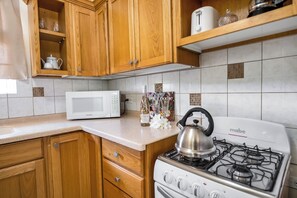 A kitchen with wooden cabinets, a white microwave, a gas stove, and a kettle. - Adulo Apartments (Rockley)