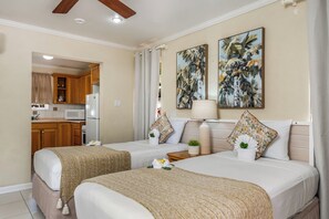 A hotel room with two beds, a kitchenette, and a painting of tropical foliage.