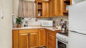 Una cocina con armarios de madera, un microondas blanco, una estufa y un lavamanos.