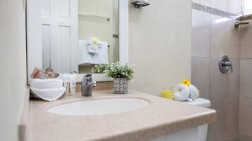 Un baño con lavamanos, espejo, artículos de aseo, una planta en maceta y cabina de ducha.