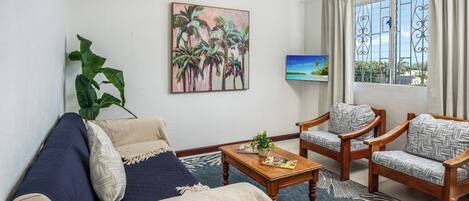 A living room with a sofa, two armchairs, a coffee table, and a painting of palm trees.