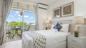 A hotel room with a bed, bedside tables, a balcony with a table and chairs, and a view of greenery.