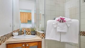 Casa de banho com cabine de duche em vidro, lavatório com espelho e toalha com flores.