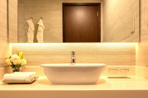 A bathroom with a white sink, a mirror, a towel rack with towels, and a wooden door. - Fraser Suites Seef Bahrain (Manama)
