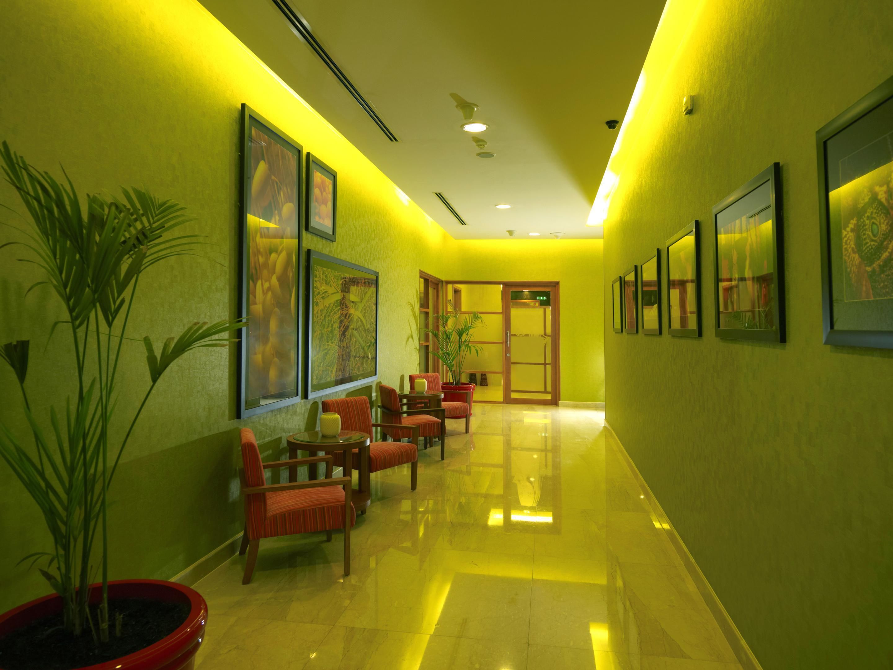 A hotel lobby with a long corridor, chairs, potted plants, and framed artwork on the walls.