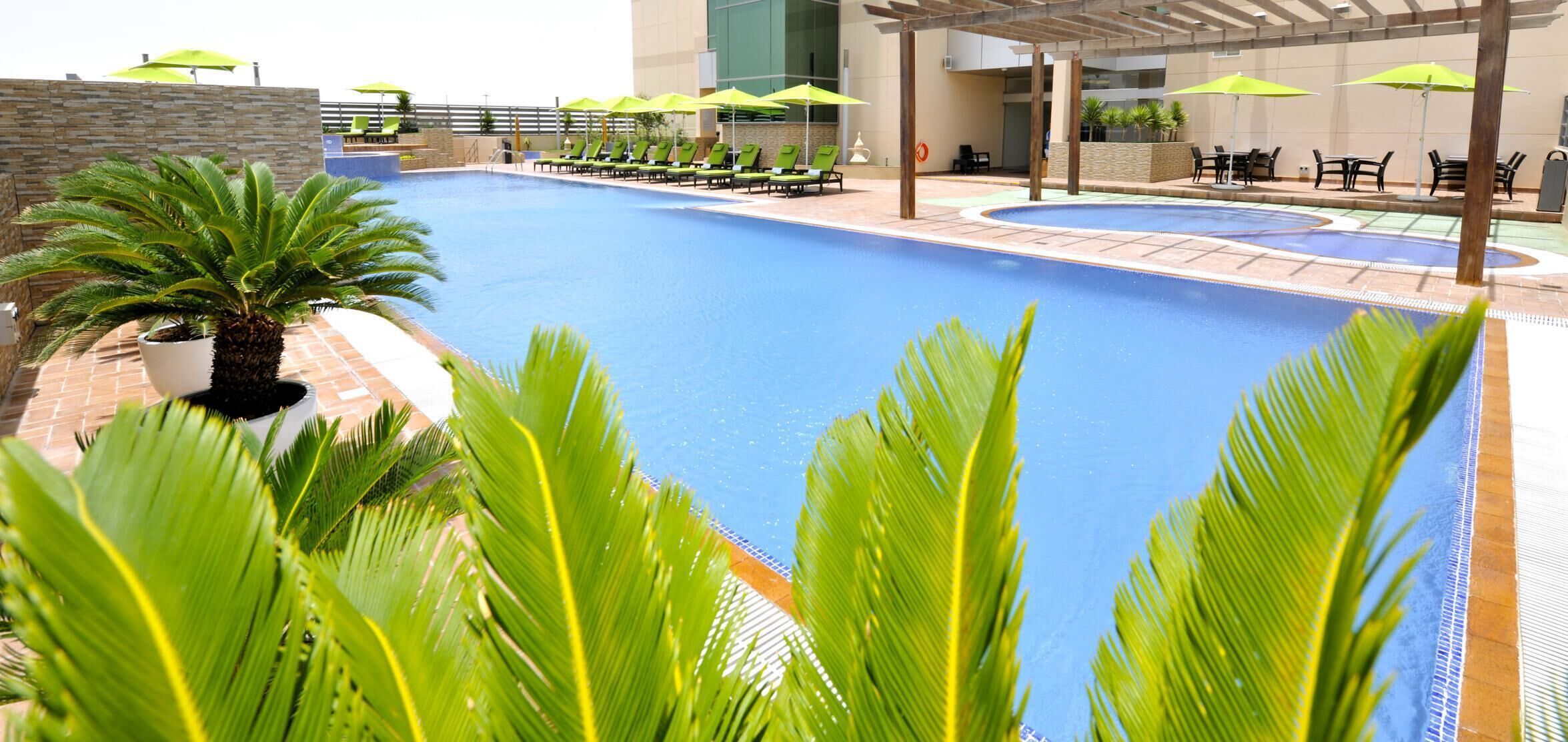 Ein Pool mit Liegestühlen und Sonnenschirmen, umgeben von Palmen und einer Pergola.