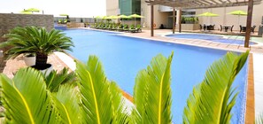 A swimming pool with lounge chairs and umbrellas, surrounded by palm trees and a pergola. - Fraser Suites Seef Bahrain (Manama)