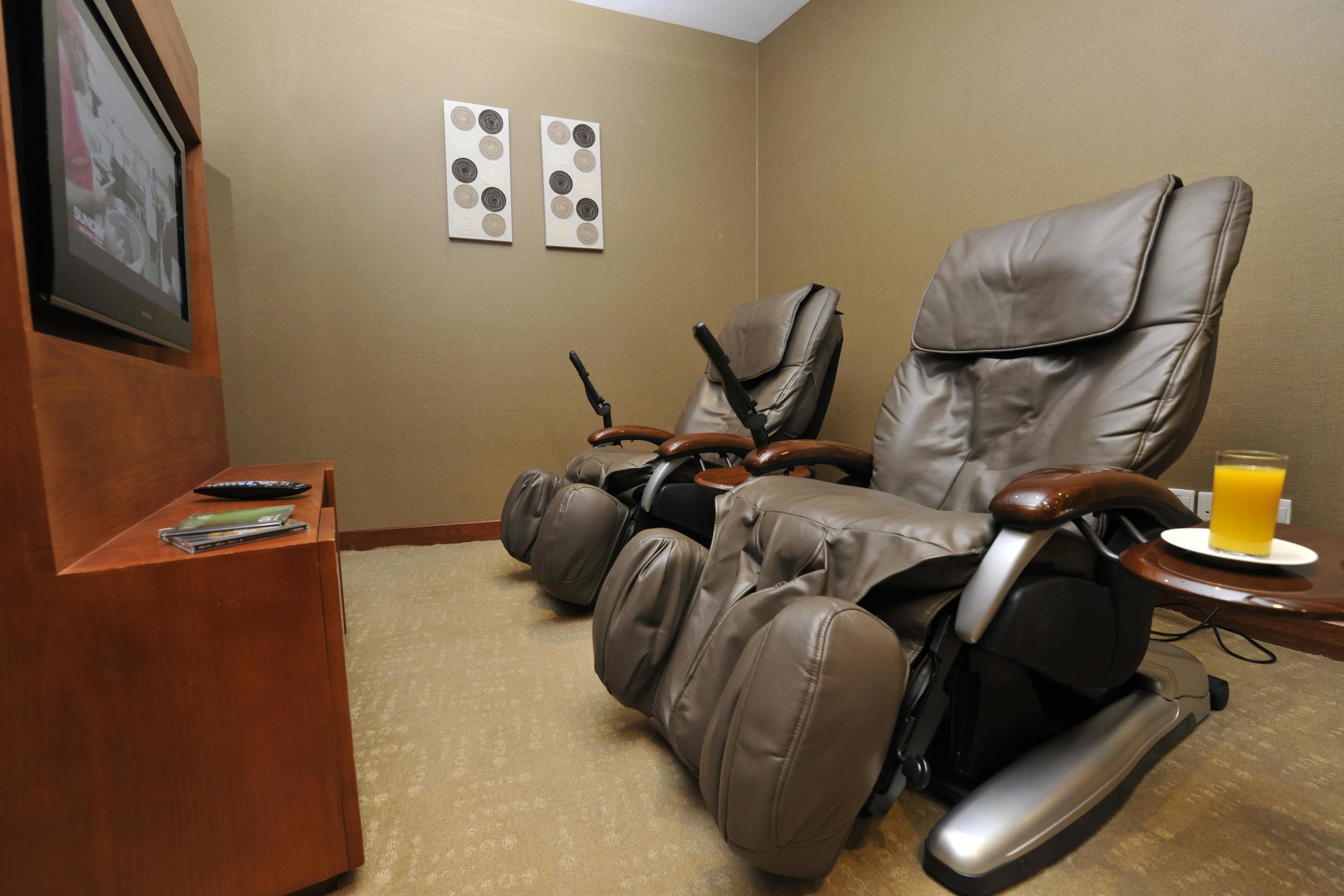 A massage chair room with a TV, two wall art pieces, and a glass of juice on a small table.